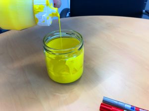 Die gelbe Acrylfarbe wird in das leere Honigglas gefüllt
